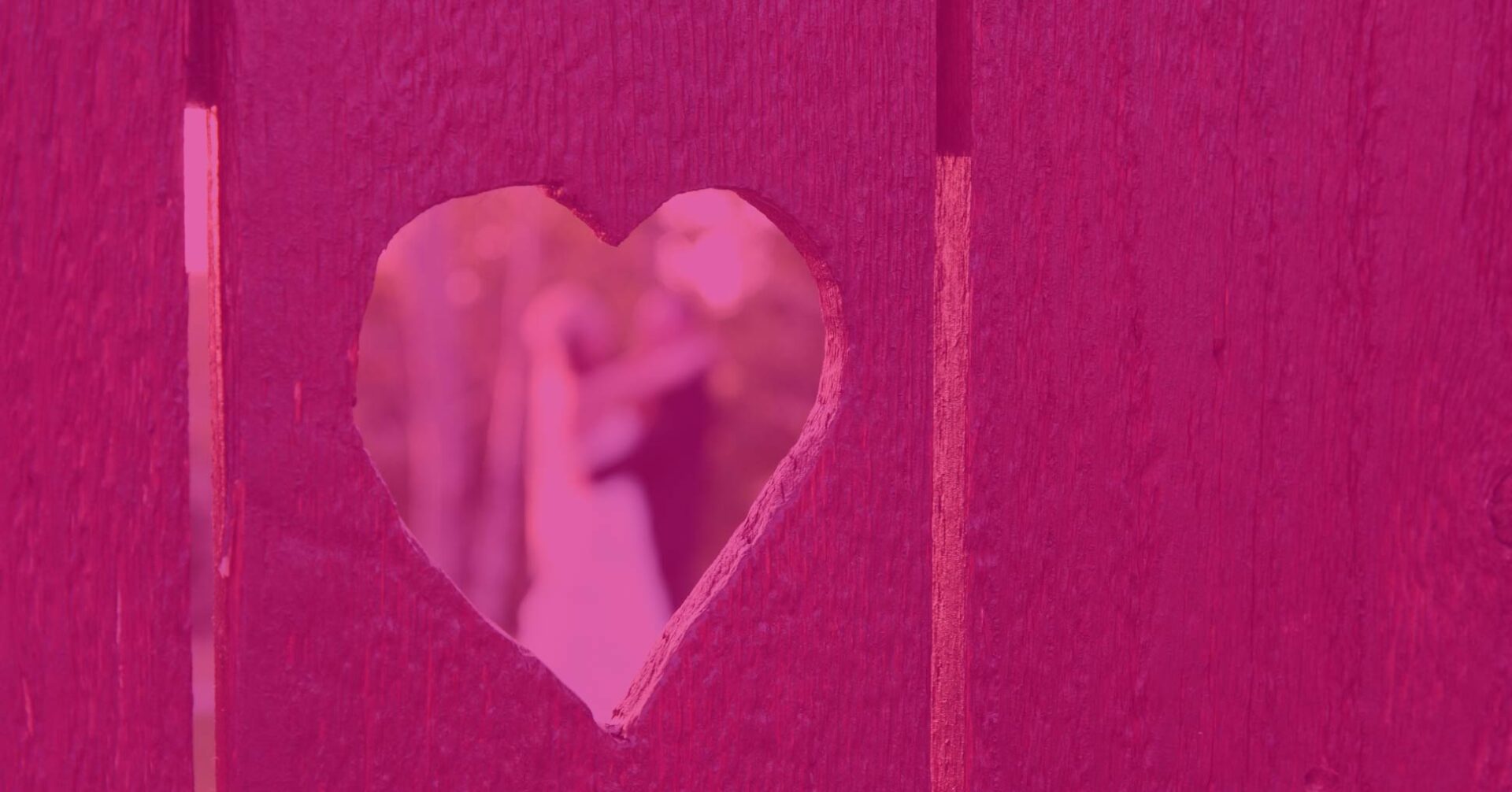 wedding couple kissing as seen through heart shaped cut in wood fence